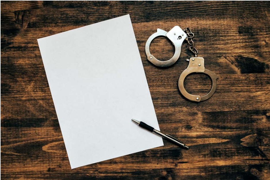 Une feuille blanche, un stylo et une paire de menottes sur un bureau en bois, représentant un rapport de police dans une affaire de conduite avec facultés affaiblies.