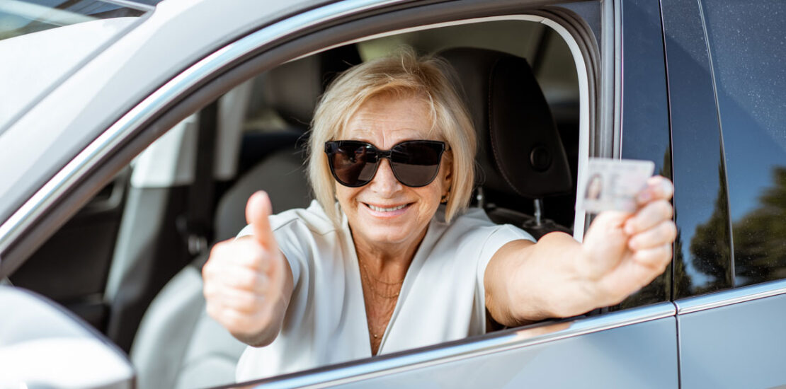Une femme plus âgée assise joyeusement au volant en tenant son permis restreint, après qu'il a été suspendu pour conduite avec facultés affaiblies.