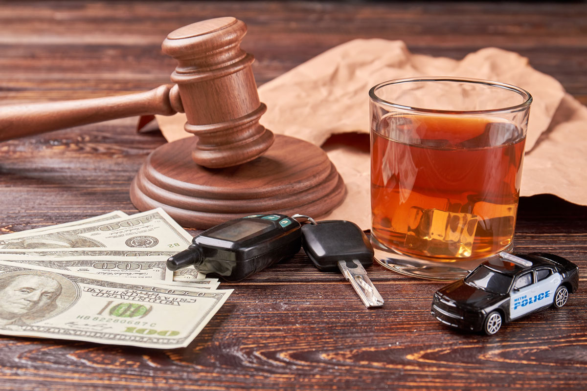 Argent, clés de voiture, une voiture de police-jouet et un verre d'alcool sur une table avec le maillet du juge, représentant les risques de l'alcool au volant.