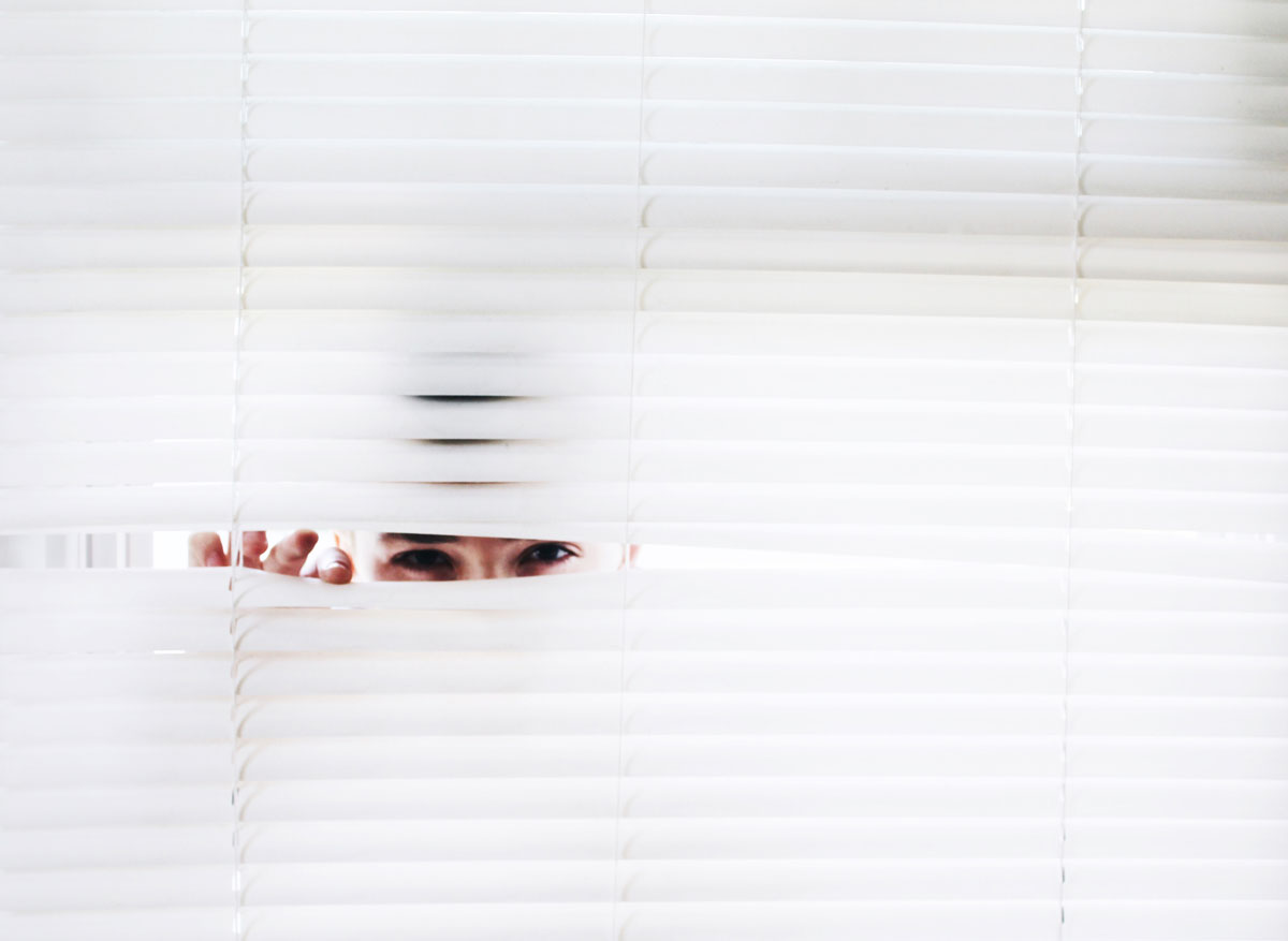 A man peeping through white blinds, suggesting the need for a criminal lawyer for voyeurism.