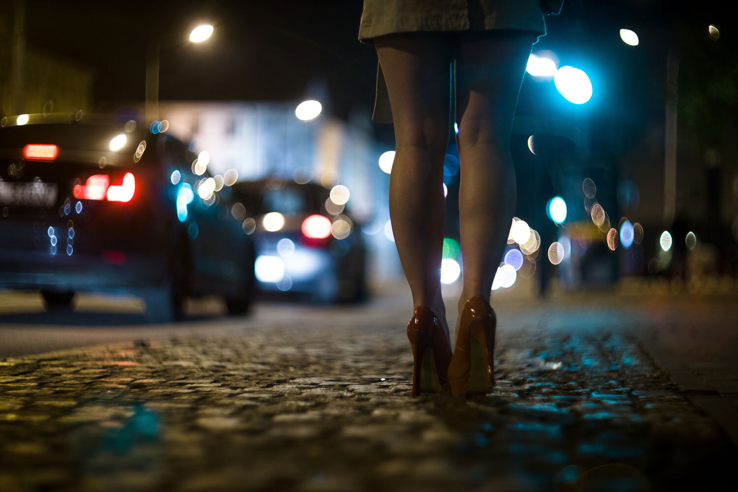A woman standing in red heels on the sidewalk with cars passing, suggesting the need for a criminal lawyer for sexual activities.